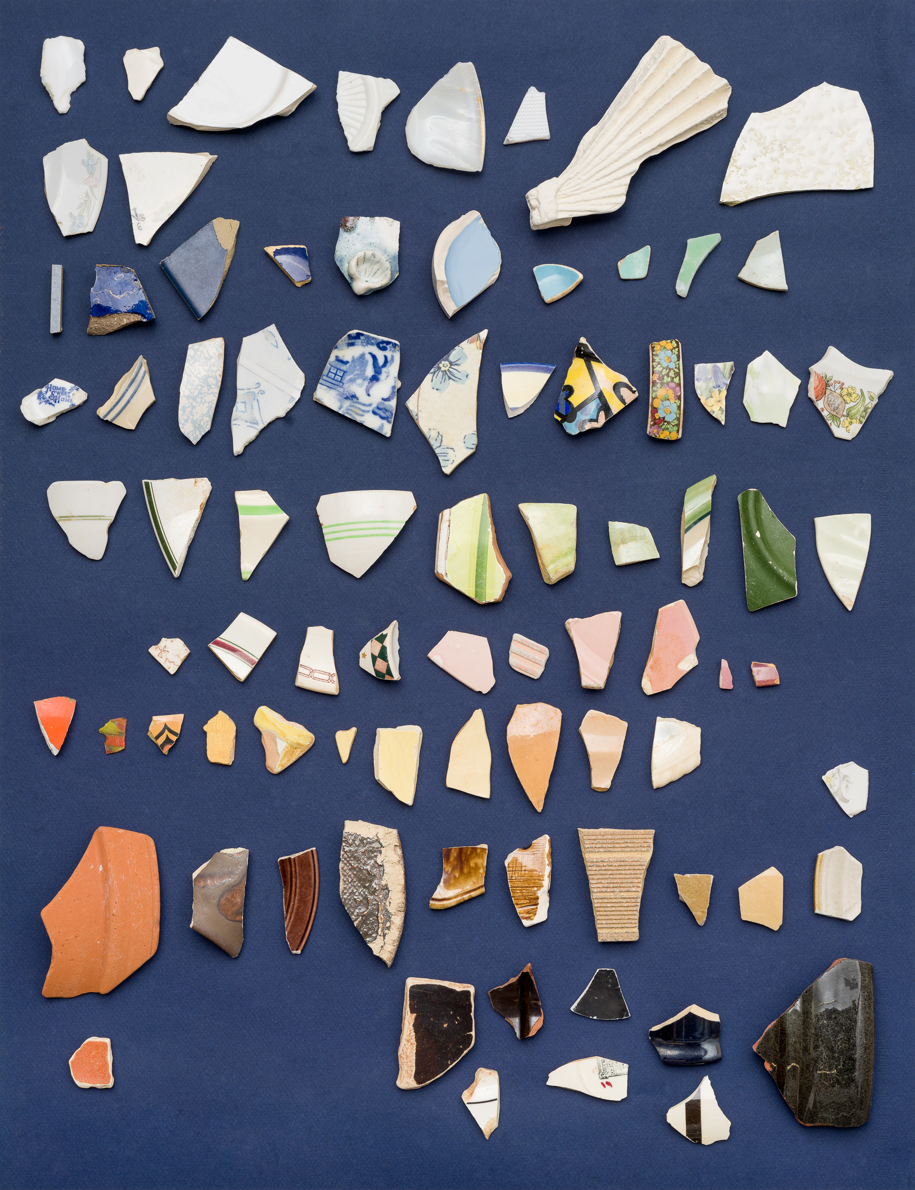 Multicoloured shards of broken pottery arranged in rows agaisnt a navy blue background. 